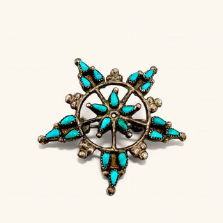 A silver-toned snowflake-style brooch featuring multiple turquoise-colored stone accents, photographed on a plain off-white background.