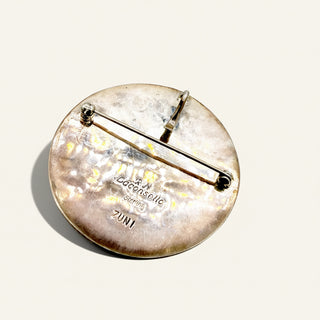 Round metal brooch with engraved text on a white background
