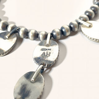 Silver beaded necklace with circular pendants on a white background