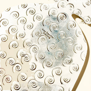 Close-up of silver jewelry spiral pattern and 'Alex Sanchez engraving.