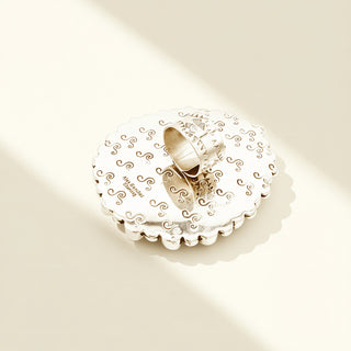 Silver ring on a decorative white stand with intricate patterns on a beige background