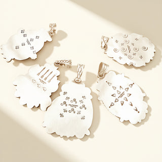 Five silver stamp pendants on a beige background