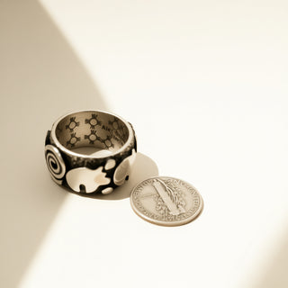 Silver ring with engraved design next to a coin on a beige background