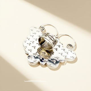 Silver cloud-shaped pendant with intricate designs on a beige background