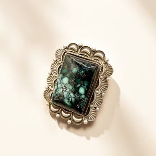 Ring with a green stone and decorative band on a beige background