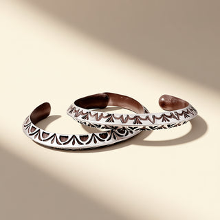 Two silver cuffs with intricate designs on a beige background