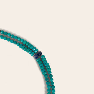 Turquoise beaded necklace with a blue clasp on a light beige background