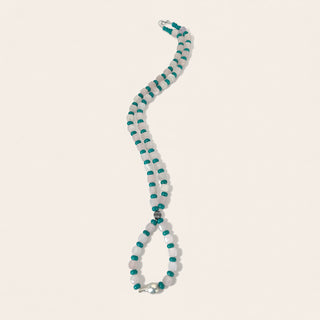 Necklace with white and teal beads on a beige background