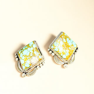 Pair of earrings with turquoise and gold design on a beige background