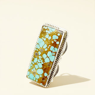 Turquoise and gold ring with silver band on a beige background