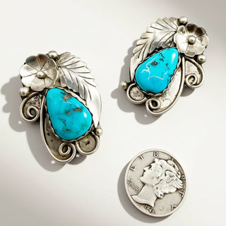Pair of silver earrings with turquoise stones and a coin for scale on a white background