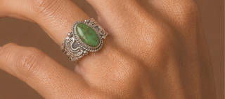Silver ring with a green stone on a person's finger against a brown background