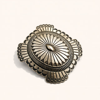 Decorative silver brooch with intricate design on a white background