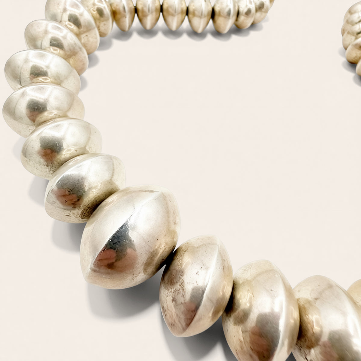 A close-up of a metallic beaded necklace or bracelet with large, polished silver-toned oval beads on a plain light background.
