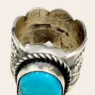 A sterling silver ring featuring a large, vibrant turquoise stone in a bezel setting, photographed against a light beige background.