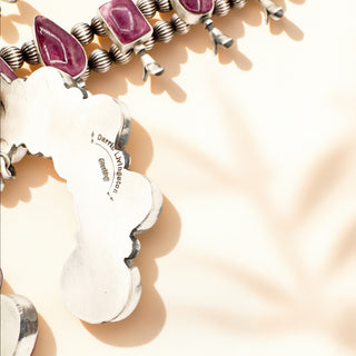 Close-up of a necklace with purple gemstones and silver accents on a soft beige background.
