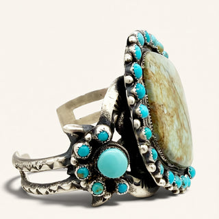 A silver-toned Southwestern-style ring featuring a large oval turquoise stone and multiple smaller round turquoise accents, photographed on a clean off-white background.