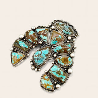 A Southwestern-style silver pendant featuring multiple turquoise and brown matrix stones, accented with small white beads, on a light beige background.
