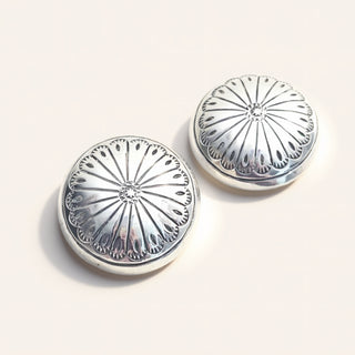 Pair of silver round earrings with intricate designs on a light background