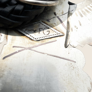 a close up of a sterling silver jewelry piece with an engraved stamp on a beige background