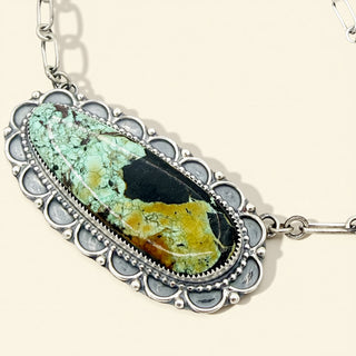 Necklace with a pendant featuring a green and black stone on a beige background