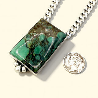 Necklace with a green stone pendant next to a coin for scale on a white background