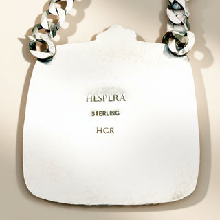 White stone with 'Hespera Sterling HCR' engraving and silver chain on beige background