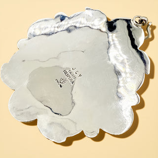 Silver stamp pendant with "JCV Hespera' on a beige background