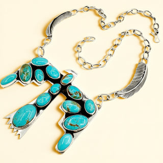 Silver bird necklace with turquoise stones on a beige background