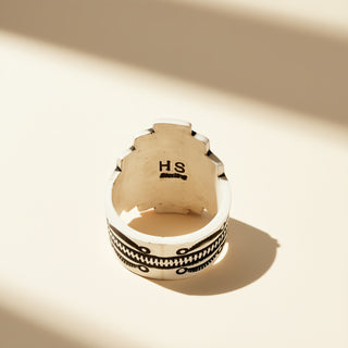 Silver ring with 'HS' initials on a beige background