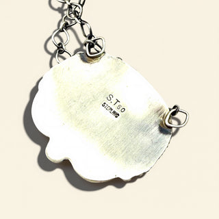 Silver pendant with 'S.T.so' branding on a beige background
