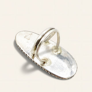 A sterling silver ring designed to look like a vintage slide sandal, featuring a textured oval base and a double-band loop, shown on a light cream background.