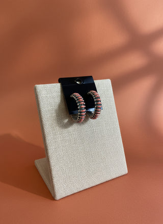 Two coral colored earrings on a black stand on a wooden surface