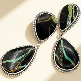 Teardrop-shaped earrings with black and green marbled stones on a beige background
