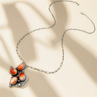 Necklace with a unique pendant featuring orange stones on a beige fabric background