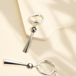 Pair of silver hoop earrings with cylindrical charms on a beige background