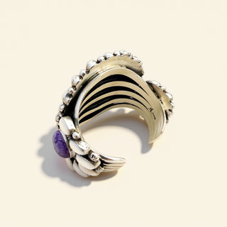 Decorative cuff with black and white pattern and purple gemstone on a beige background