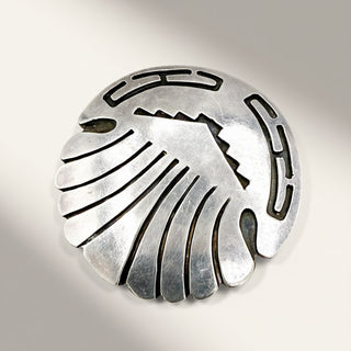 A round sterling silver brooch featuring a stylized Native American eagle design with cutout details, displayed on a neutral light gray background.
