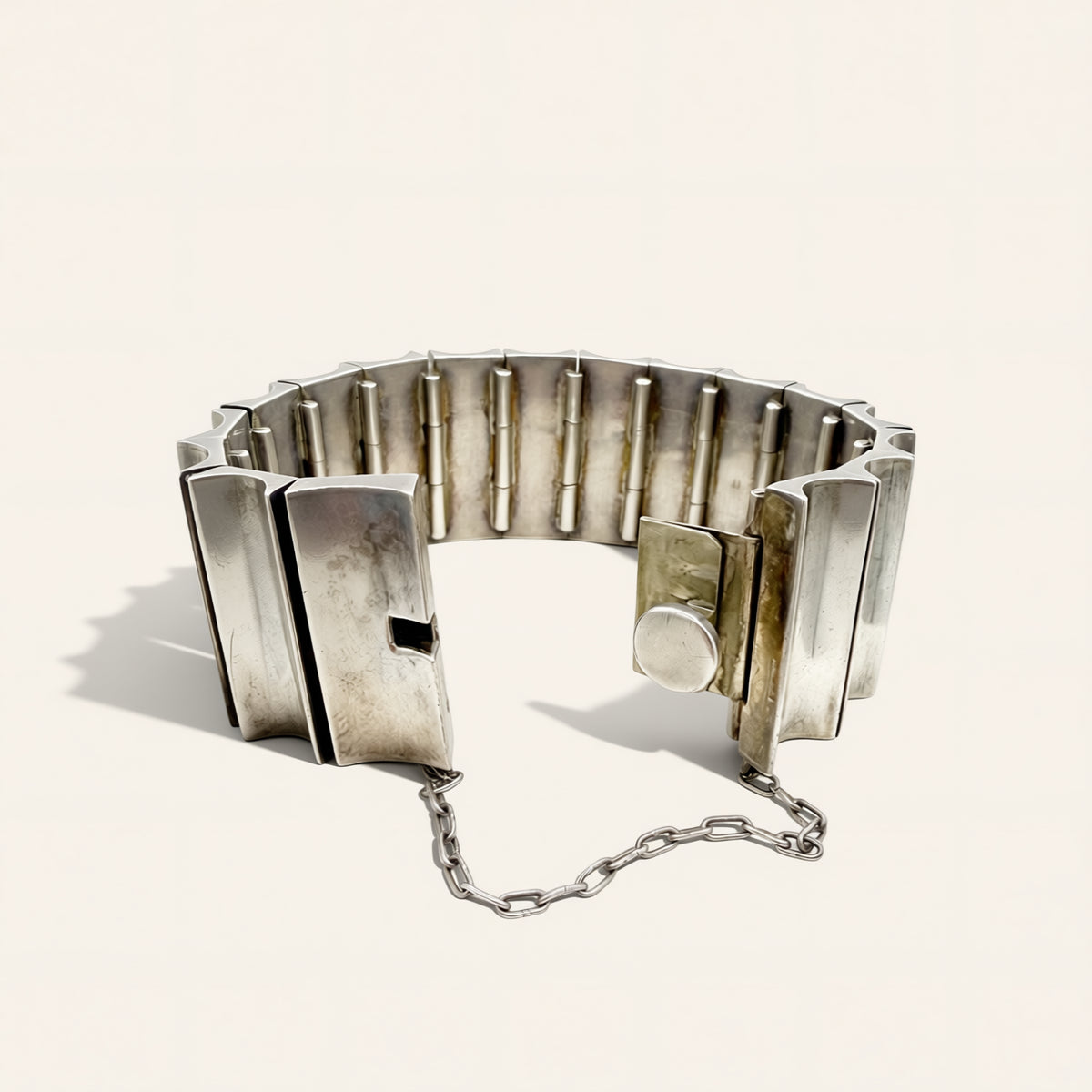 A silver metal link-style bracelet with a unique geometric segmented design, featuring a short chain attached near the clasp, photographed on a clean off-white background.