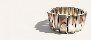 A metallic silver band bracelet with a segmented, accordion-like design, shown on a plain off-white background with a soft shadow.