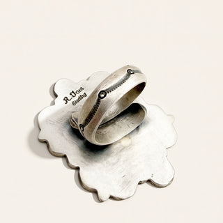 A sterling silver ring with a textured,  engraving on it, set against a plain off-white background.