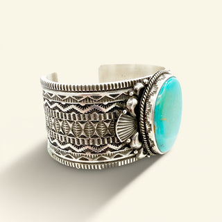 Silver bracelet with intricate patterns and a turquoise stone on a light background