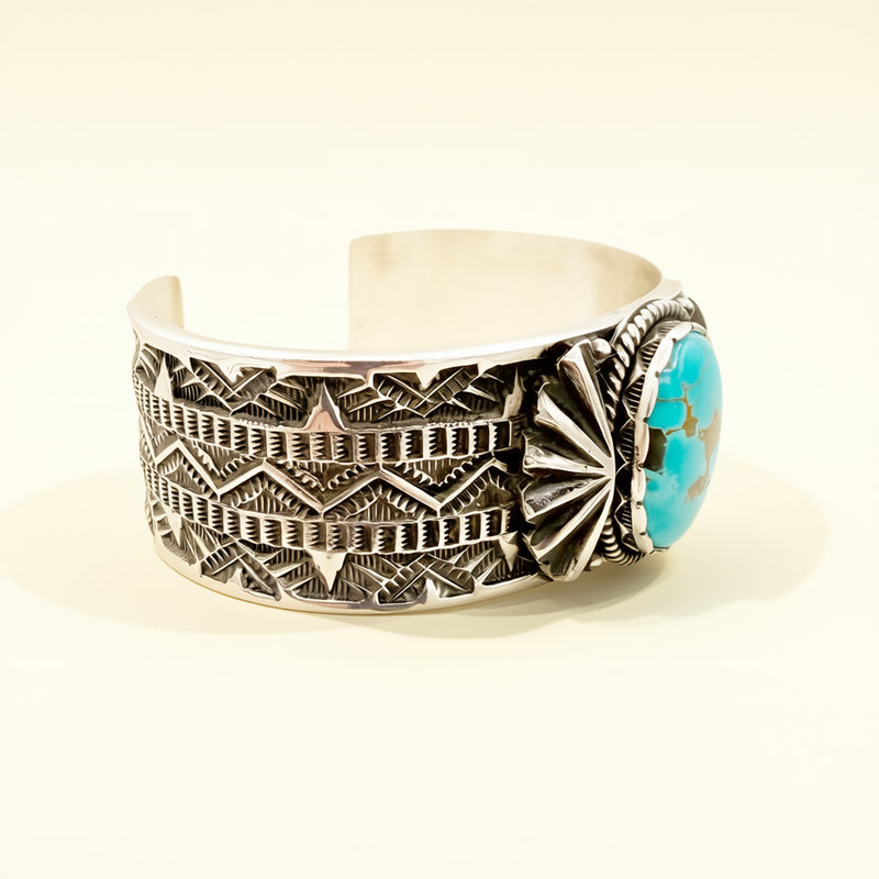 Silver cuff bracelet with intricate patterns and a turquoise stone on a light background