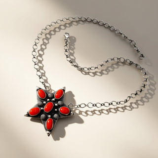 Star-shaped pendant with red stones on a silver chain against a beige background