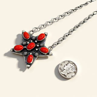 Star-shaped silver pendant with red stones on a chain, featuring a coin charm, on a light background.