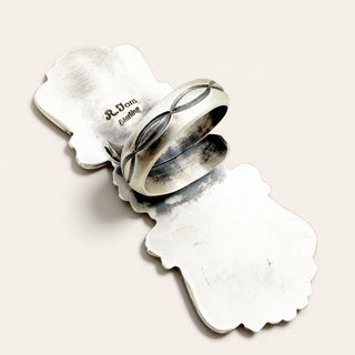 A sterling silver ring with an infinity symbol design, displayed on a matching sterling silver stand against a light beige background.
