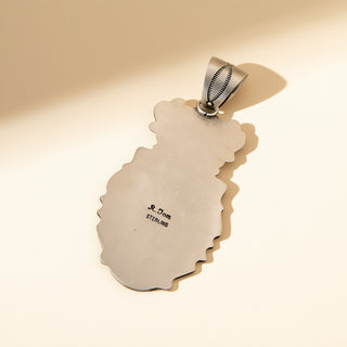 Silver pendant with 'R. Tom' engraving on a beige background