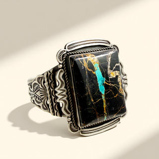 Silver cuff with a rectangular stone featuring black, gold, and turquoise patterns on a beige background.