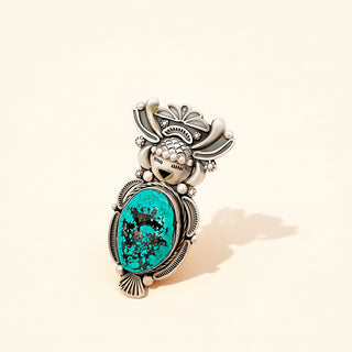 Decorative ring with turquoise stone and black design on a beige background