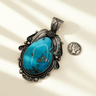 Turquoise pendant with intricate silver design on a beige background